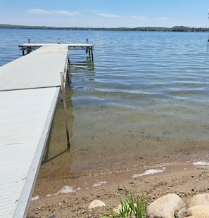 A wooden dock extending into a calm lake with clear water, surrounded by a natural landscape. - The Hideaway on Detroit Lake (Detroit Lakes)