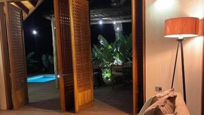 An open living area with a sofa, pillows, a lamp, and a view of an outdoor pool area at night. - Private Villa with Pool and Gardens (Palomino)