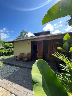 Ein Haus mit einer überdachten Veranda, zwei Holzstühlen und einer großen Bananenpflanze im Vordergrund.
