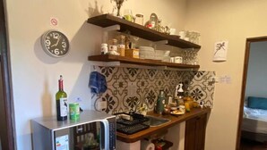 Una cocina equipada con microondas, refrigerador y estantes con vajilla y botellas.