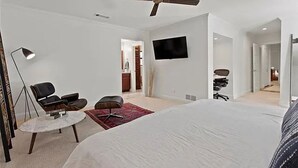 Een slaapkamer met een bed, twee stoelen, een bureau, een televisie en een plafondventilator.