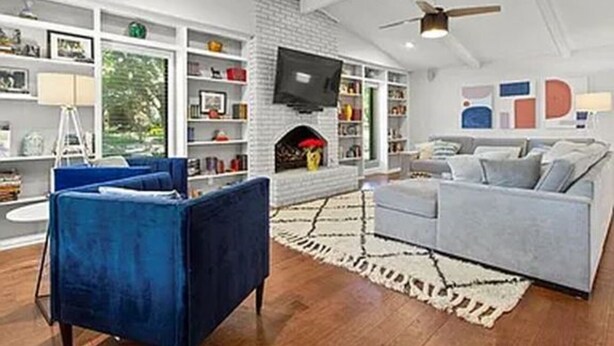 Een moderne woonkamer met een open haard, een blauwe fauteuil, een grijze bank en een boekenkast.