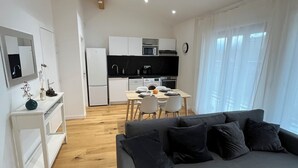 A modern living space with a grey sofa, wooden flooring, a white console table, and a kitchen area with white cabinets and appliances. - Apartment Camille Pujol Toulouse (Toulouse)