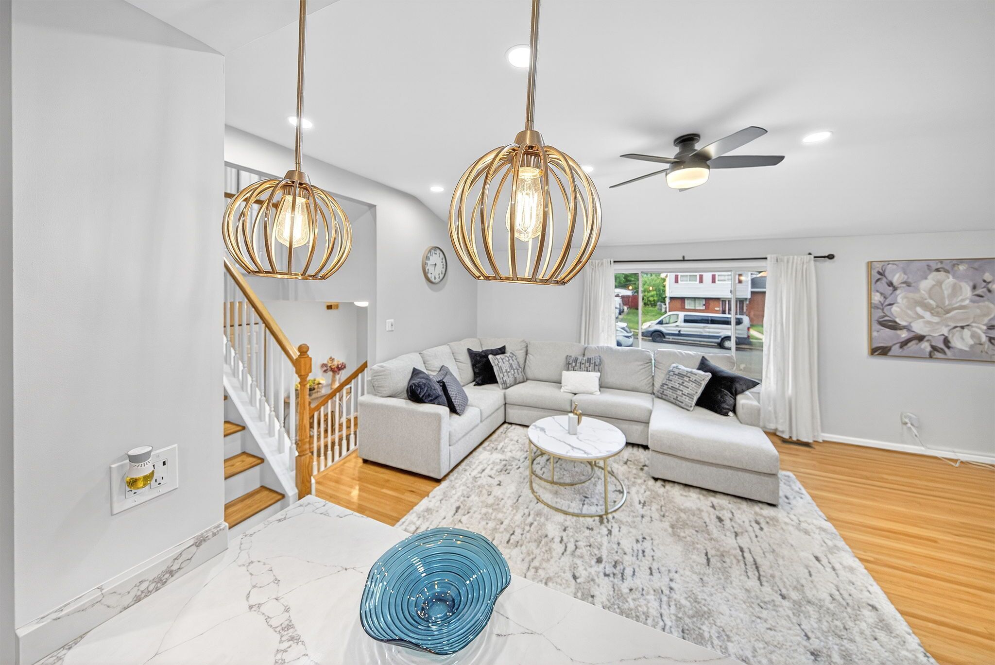 A modern living room with a sectional sofa, a marble coffee table, and a staircase.
