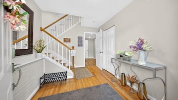 A modern hallway with a wooden staircase, a white door, a metal console table with flowers, and a gray rug.