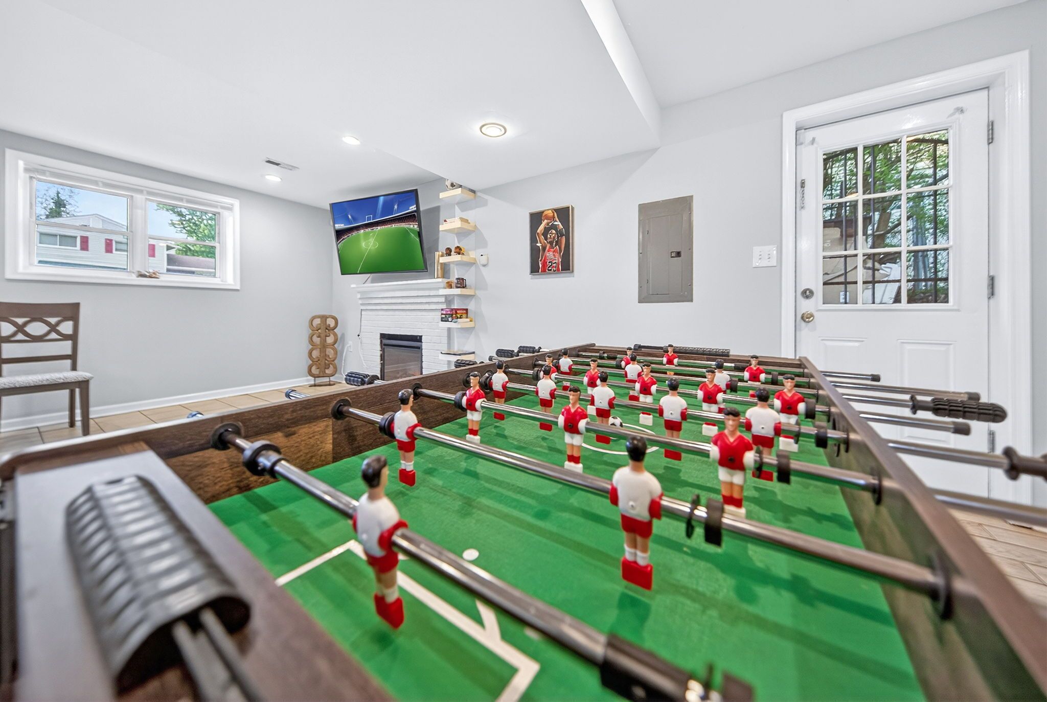 Una habitación con mesa de fútbol de mesa, televisor montado en la pared y ventana con vista a edificios.