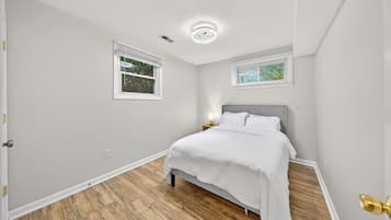 A bedroom with a bed, two windows, a nightstand, and a ceiling light.
