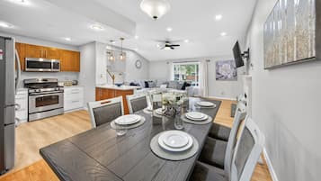 Una cocina moderna con electrodomésticos integrados, un comedor con una mesa de madera preparada para seis personas y un ventilador de techo.