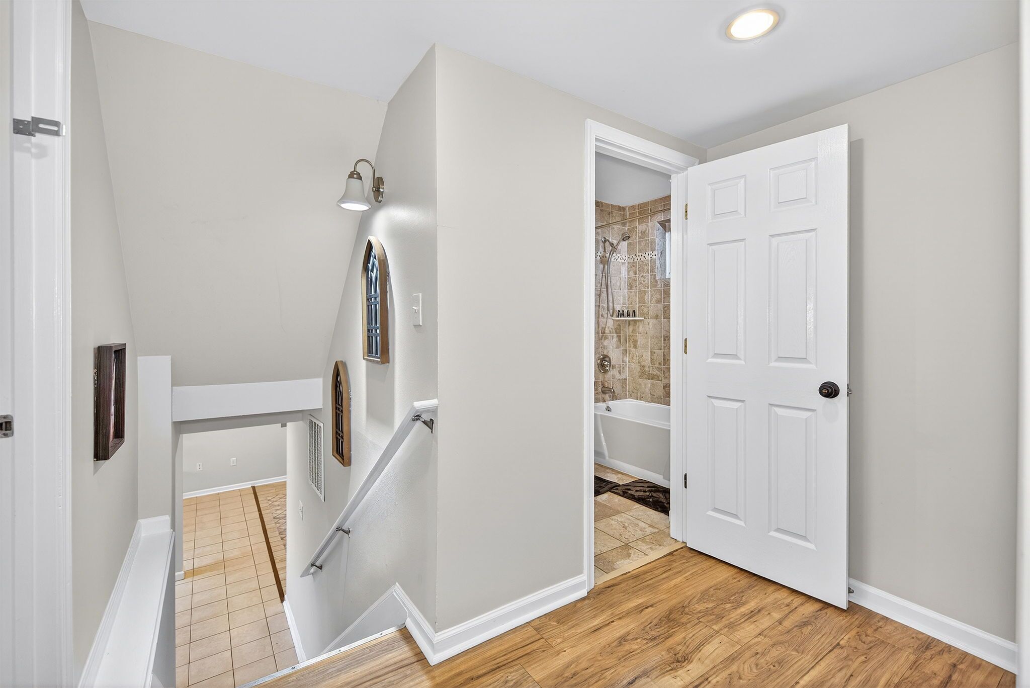 A hallway with a wooden floor, a white door, and a shower area with tiled walls.