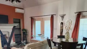 Ein Wohnzimmer mit einer Couch, einem Esstisch mit Stühlen, einem Deckenventilator und einem Kamin.
