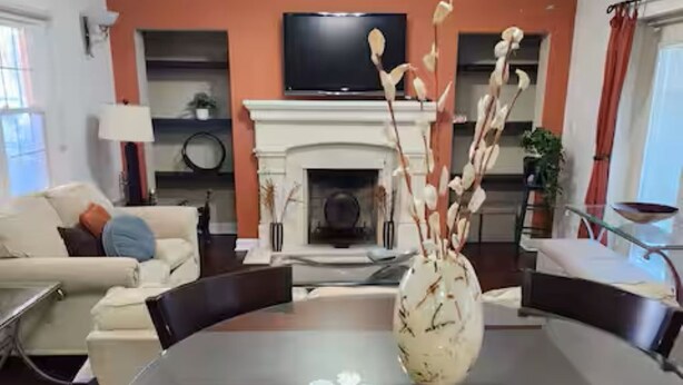 Ein modernes Wohnzimmer mit einem runden Glastisch, einem Kamin, einem Deckenventilator und einem an der Wand montierten Fernseher.