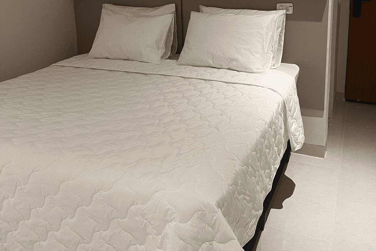 A single bed with a headboard, white bedding, and a plain wall.
