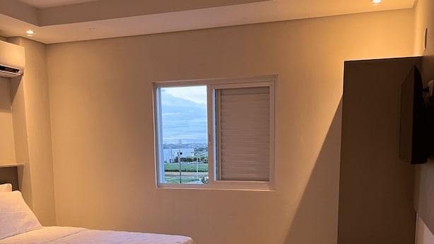 A bedroom with two beds, a window with blinds, a chair, and a television on the wall. - Hotel Blox Sorriso (Sorriso)