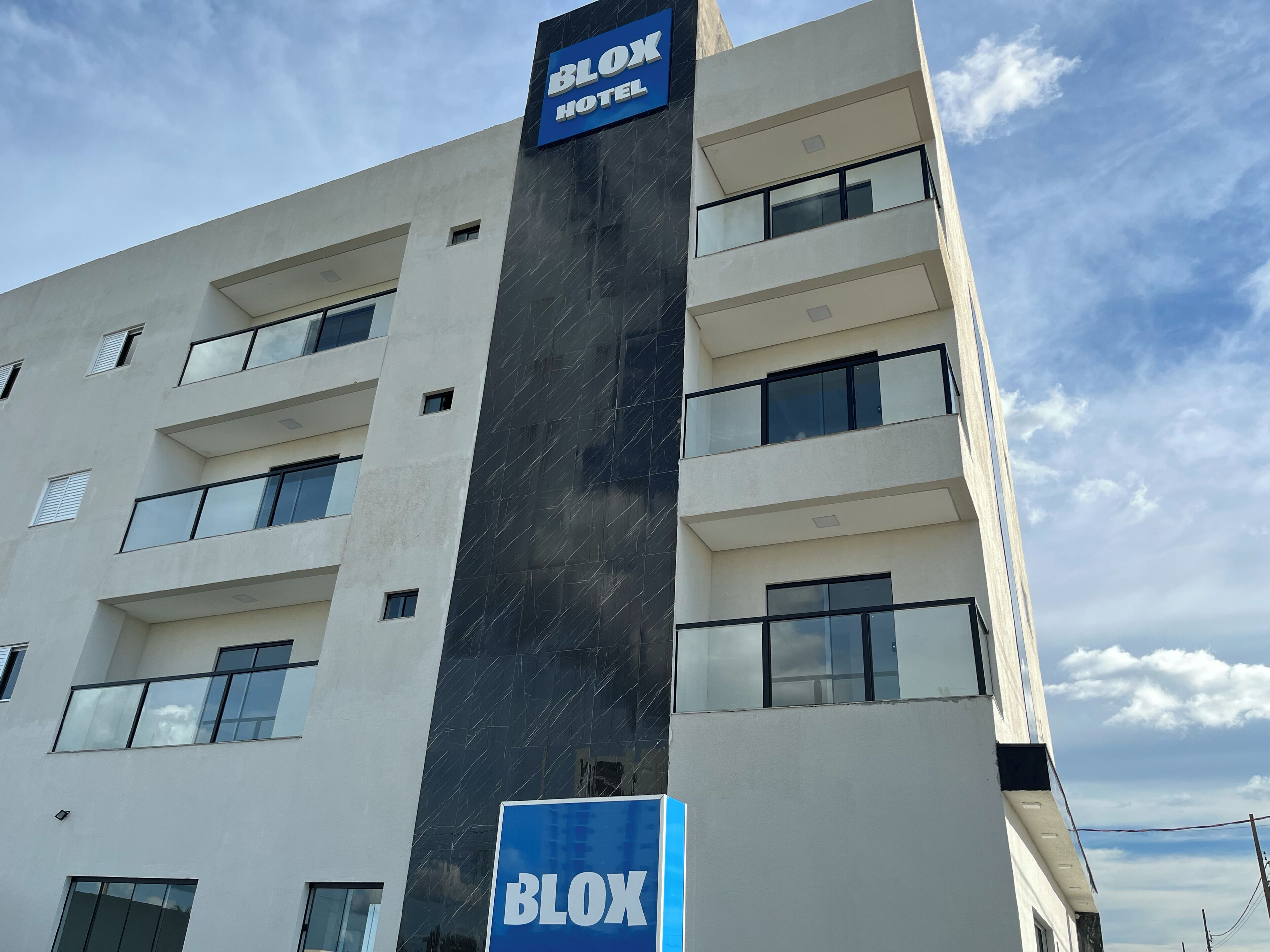 A modern hotel building with a prominent 'BLOX HOTEL' sign, multiple balconies, and a clear sky.