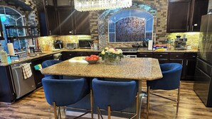 Une cuisine dotée d’un plan de travail en granit, de chaises bleues, d’un lustre et d’un pare-feu décoré d’un motif floral.