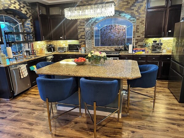 Une cuisine dotée d’un plan de travail en granit, de chaises bleues, d’un lustre et d’un pare-feu décoré d’un motif floral.