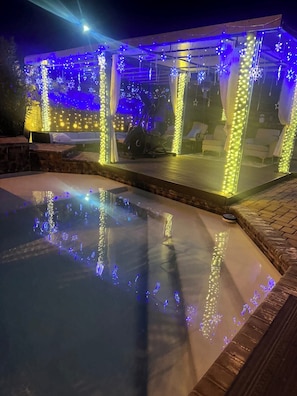 A pool with a clear water surface, surrounded by a covered area with string lights.