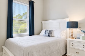 A bedroom with a bed, a nightstand, a lamp, and a window with curtains. - Gulf View Beach House / Sleeps 18 (Gulfport)