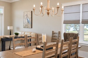 A dining area with a wooden table, chairs, a chandelier, and a painting on the wall. - Gulf View Beach House / Sleeps 18 (Gulfport)