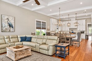 A spacious living room with a sectional sofa, a coffee table, and a dining area with a wooden table and chairs. - Gulf View Beach House / Sleeps 18 (Gulfport)