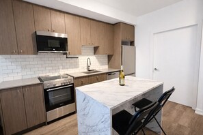 A modern kitchen with wooden cabinets, a stainless steel stove, a microwave, and a wine bottle on the counter. - Stylish Oasis Condo | Gym, Bowling, Pool, Hot Tub (Kitchener)
