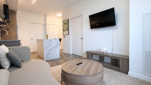 Ein modernes Wohnzimmer mit einer Couch, einem runden Couchtisch, einem an der Wand befestigten Fernseher und einer Küchenzeile mit einer Marmorinsel.