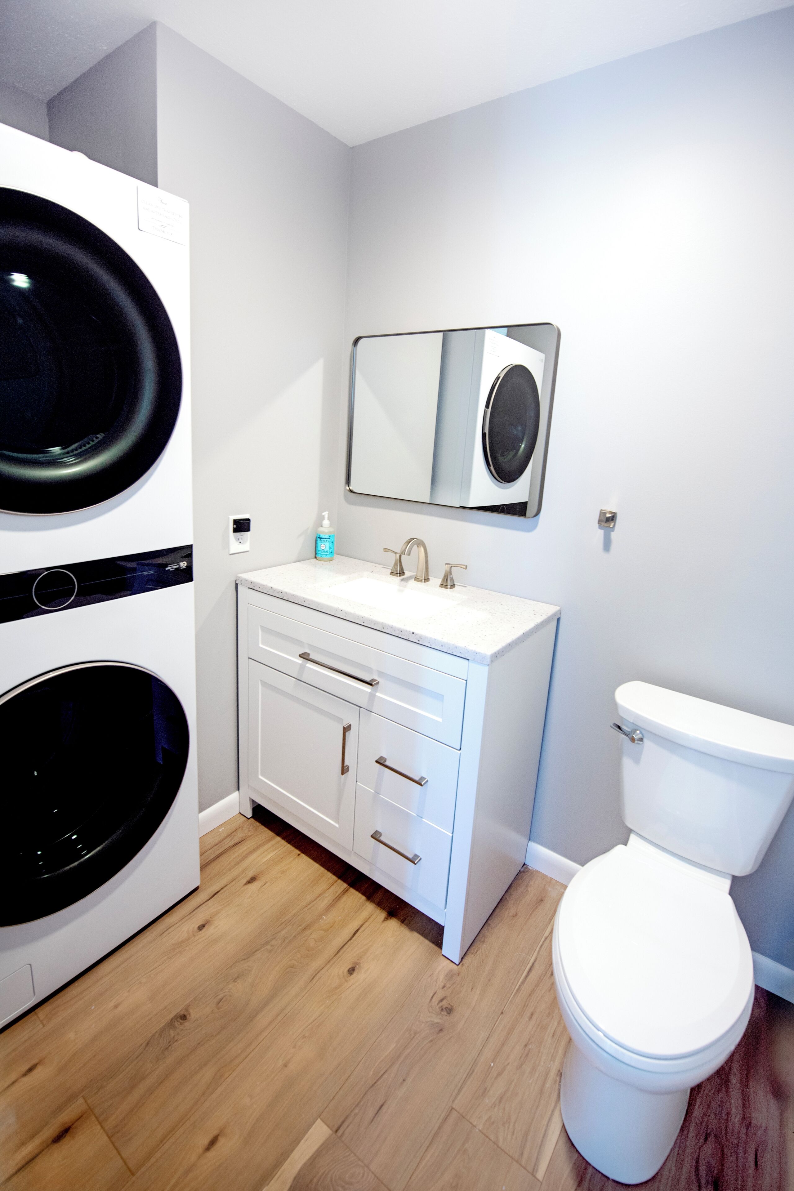 A bathroom with a white toilet, a sink with a mirror above it, and a washing machine.