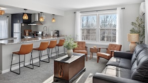 A modern kitchen with bar stools, a dining area with a sofa, and a large window. - Amherst -NEW - Campus Convenience & Social Privacy (Amherst)