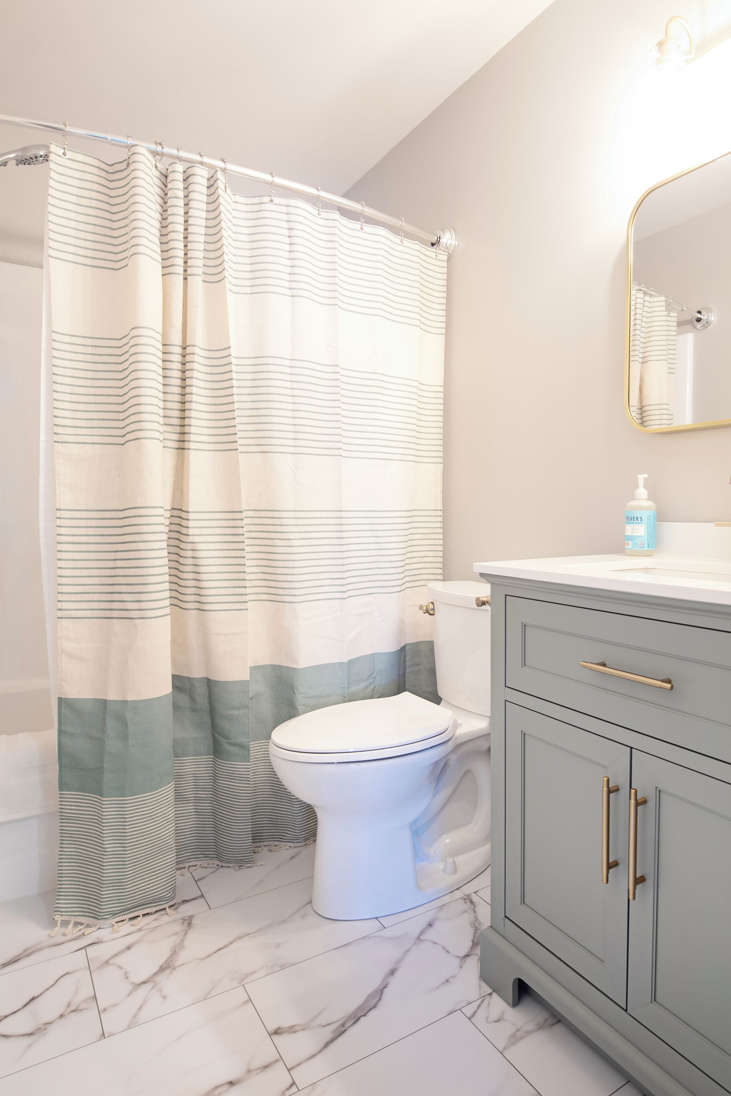 Une salle de bain avec un rideau de douche à rayures, des toilettes, un meuble-lavabo avec un miroir et un sol en marbre.