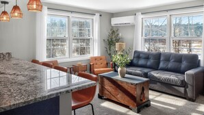 A modern living room with a large window, a leather sofa, a dining area with a marble countertop, and pendant lighting. - Amherst -NEW - Campus Convenience & Social Privacy (Amherst)