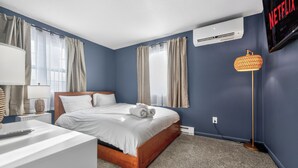 A bedroom with a bed, a bedside table, a lamp, a wall-mounted air conditioner, and a wall-mounted television. - Amherst -NEW - Campus Convenience & Social Privacy (Amherst)