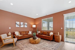 A living room with a brown sofa, a wooden coffee table, and a large window with blinds.