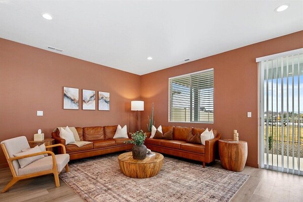 A living room with a brown sofa, a wooden coffee table, and a large window with blinds. - The Haven, Desert Inspired Retreat in Star | Zippy Wi-Fi, Sleeps 8 (Star)