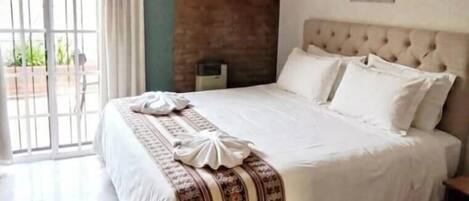 Una habitación de hotel con cama, ventilador de techo, ventana con cortinas, aire acondicionado instalado en la pared y un cuadro en la pared.