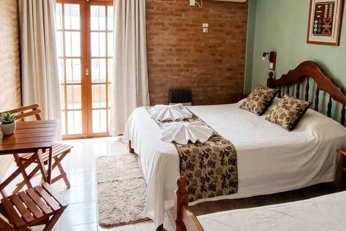 Een slaapkamer met een bed, een bureau, een stoel, een plafondventilator en een raam met gordijnen.