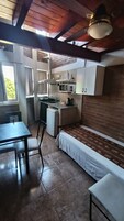 Una cocina compacta equipada con microondas, pileta y heladera pequeña. Incluye una mesa para comer con sillas y un banco.