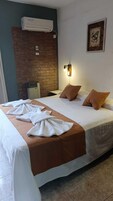 A hotel room with a bed, a brick wall, an air conditioning unit, a wall-mounted light, and a framed picture.