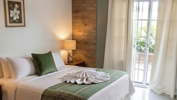 Une chambre d’hôtel avec un lit, une table de chevet, une lampe, un tableau au mur et une fenêtre avec des rideaux.