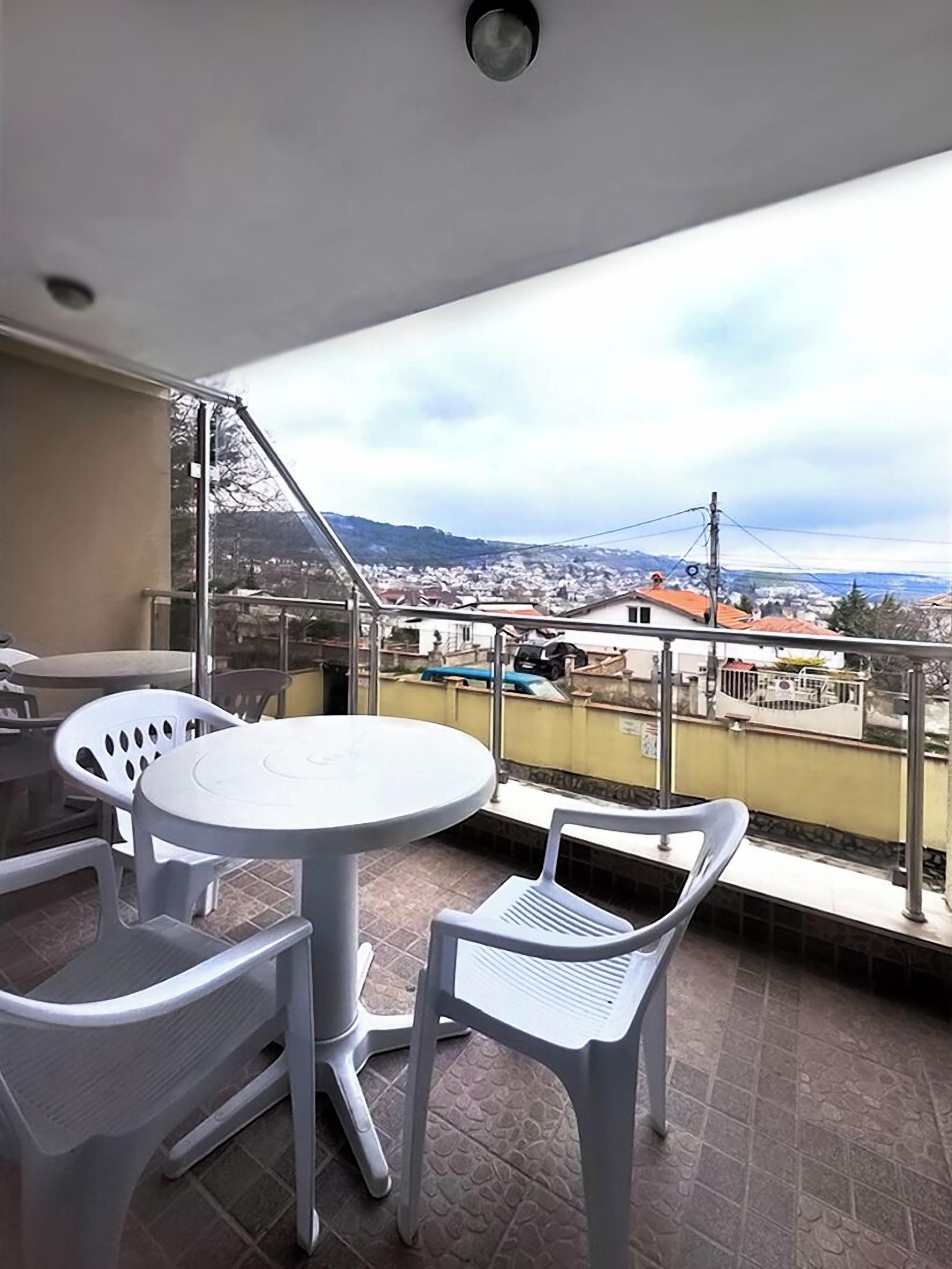 A balcony with a round table and chairs, a view of a cityscape, and a metal railing.