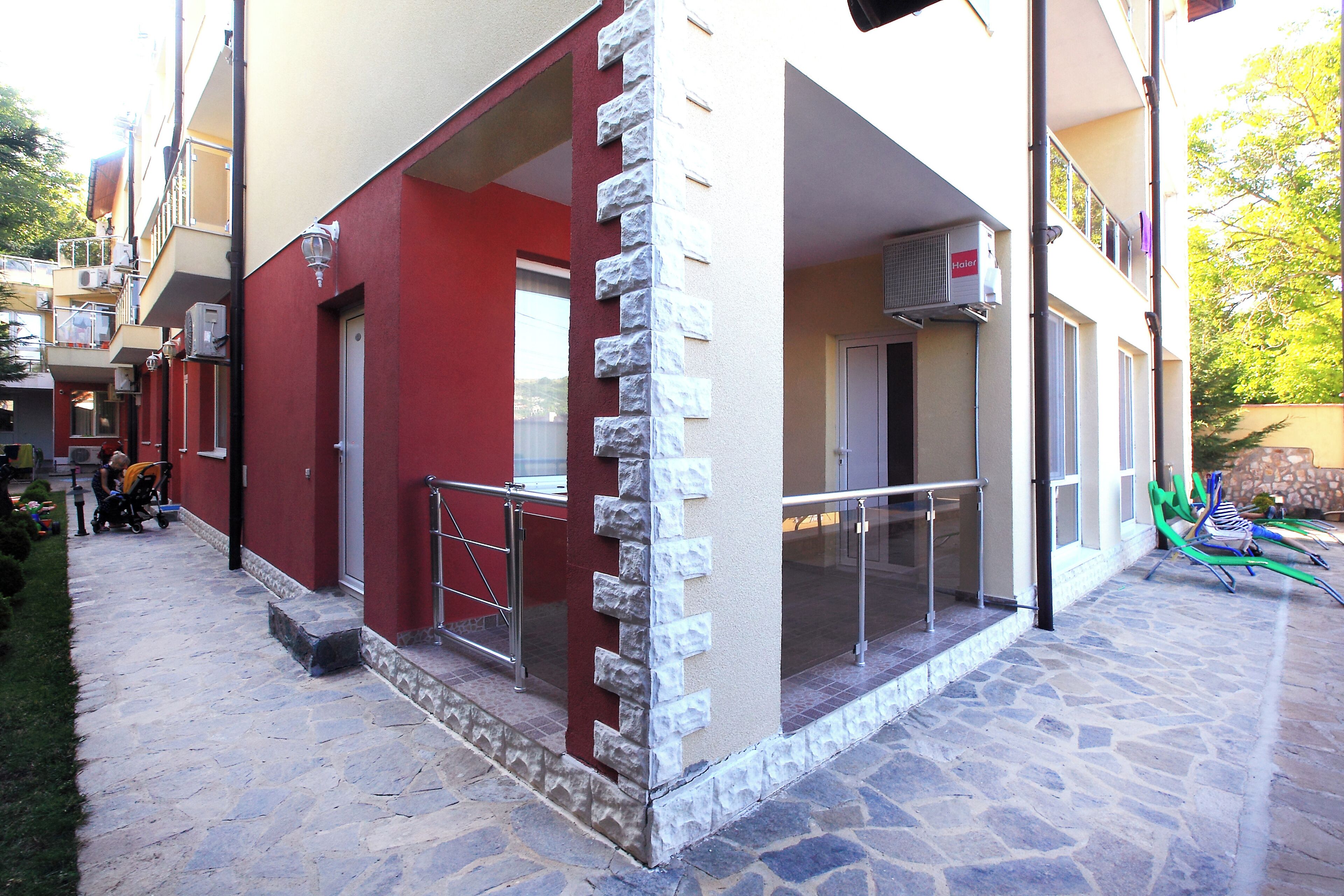 A building with a red and beige facade, a stone-paved entrance, and a balcony with a metal railing.