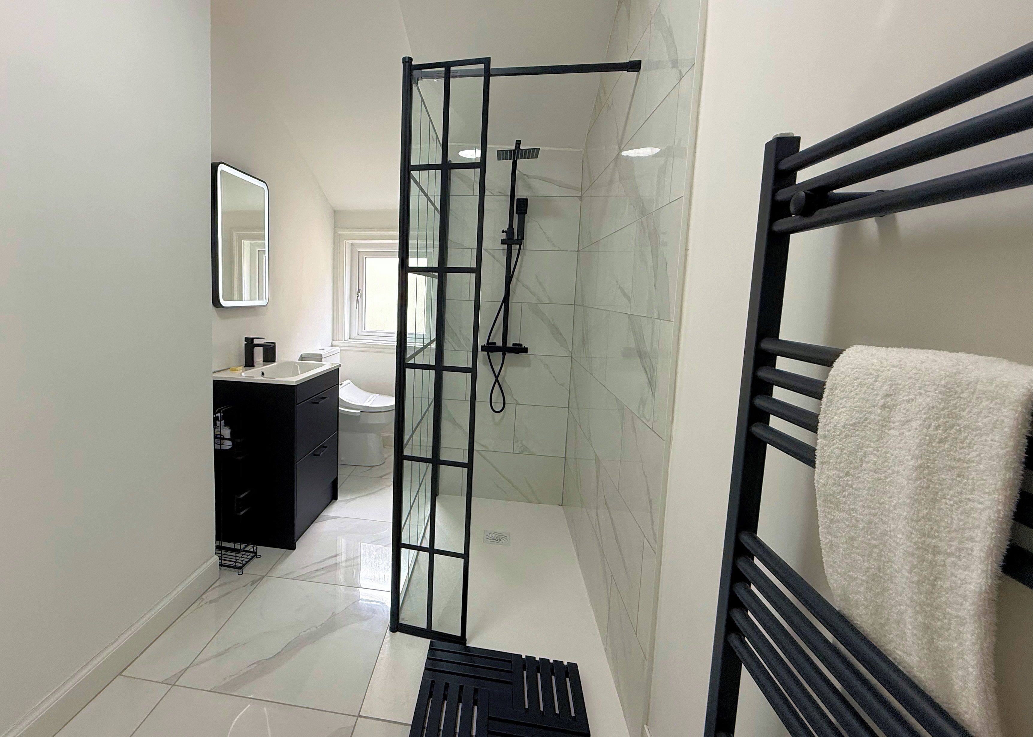 A modern bathroom with a glass shower enclosure, a black towel rack, and a white sink.