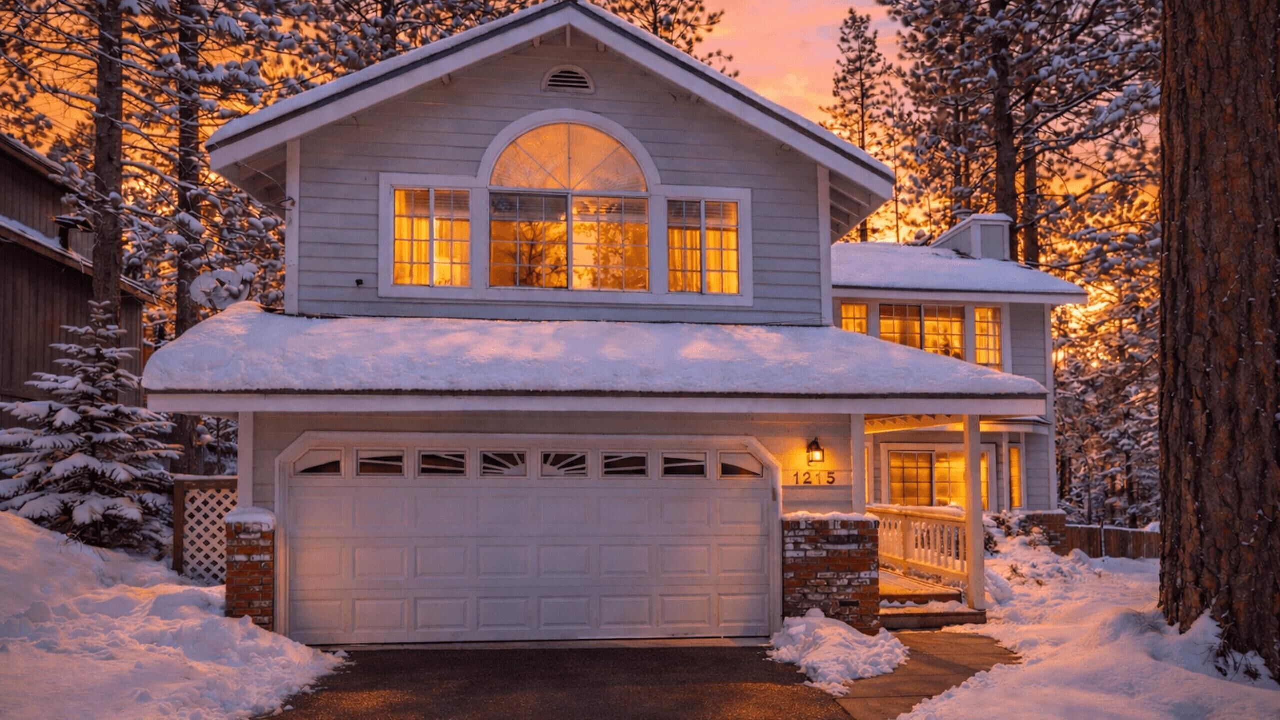 Una casa de dos pisos con garaje, rodeada de árboles cubiertos de nieve.