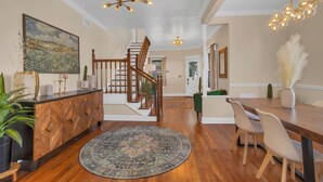 En rummelig opholdsstue med en trætrappe, et spisebord med stole og et stort billede på væggen.