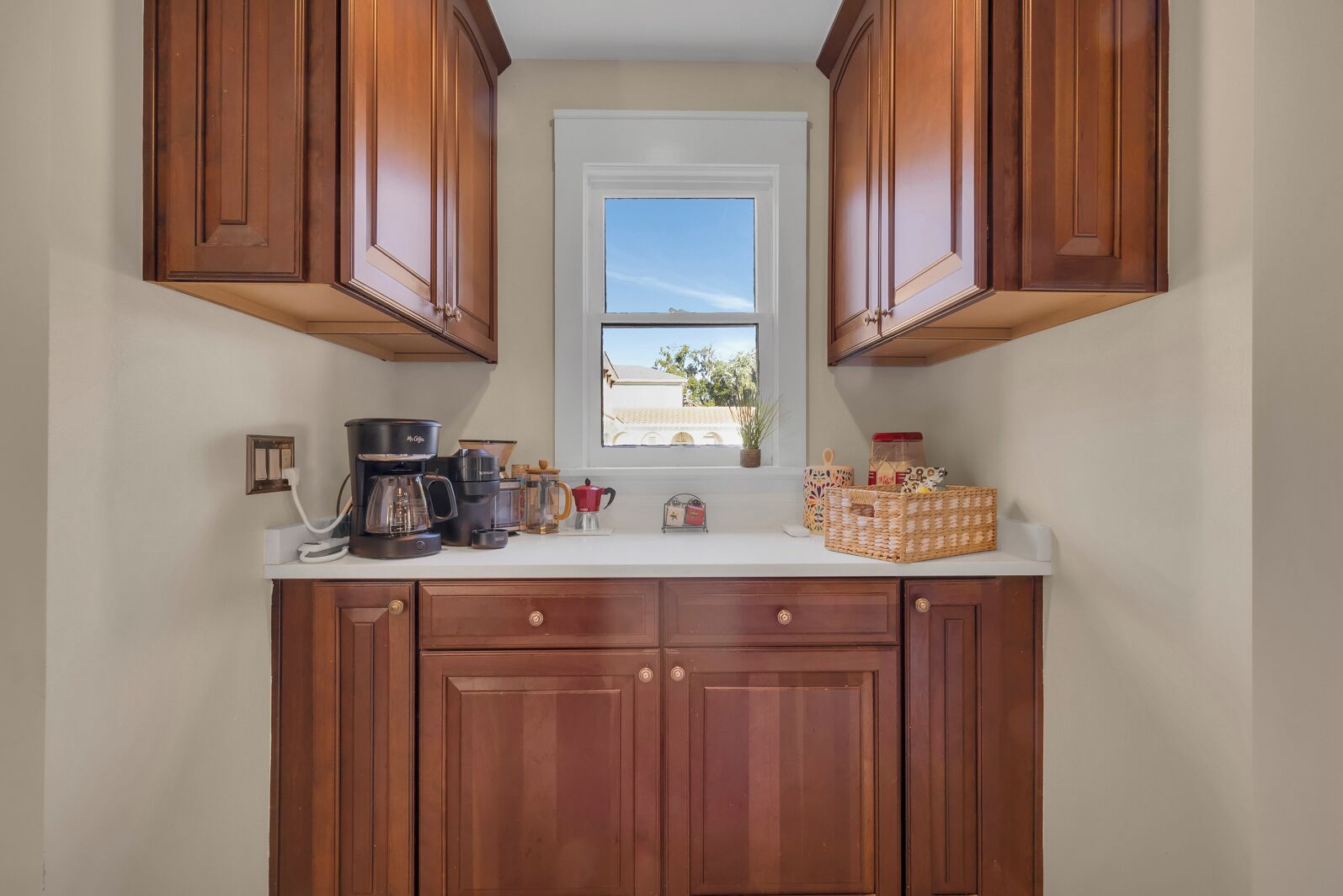 A kitchen with wooden cabinets, a coffee maker, a window with a view, and a basket on the counter.