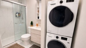 Une salle de bain avec une douche à parois de verre, des toilettes, un lavabo et des appareils de lavage superposés.