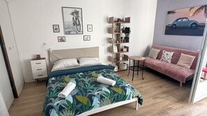 A bedroom with a bed, a sofa, a small table, a bookshelf, and a wall with pictures. - City center studio (Vendôme)
