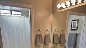 Une salle de bain équipée de toilettes, de deux lavabos, d’un rideau de douche et d’un miroir avec éclairage intégré.