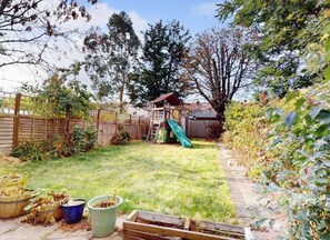 A backyard with a wooden playhouse, a slide, and a fenced area. - Stunning period property. 15 min train central London/Gatwick. (Croydon)