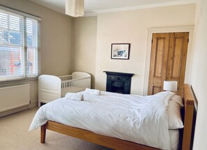 A bedroom with a bed, a crib, a radiator, a fireplace, and a door. - Stunning period property. 15 min train central London/Gatwick. (Croydon)