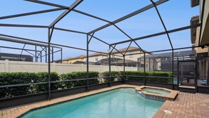 Une piscine entourée d’une paroi en verre, bordée d’une terrasse en briques et d’une clôture blanche.